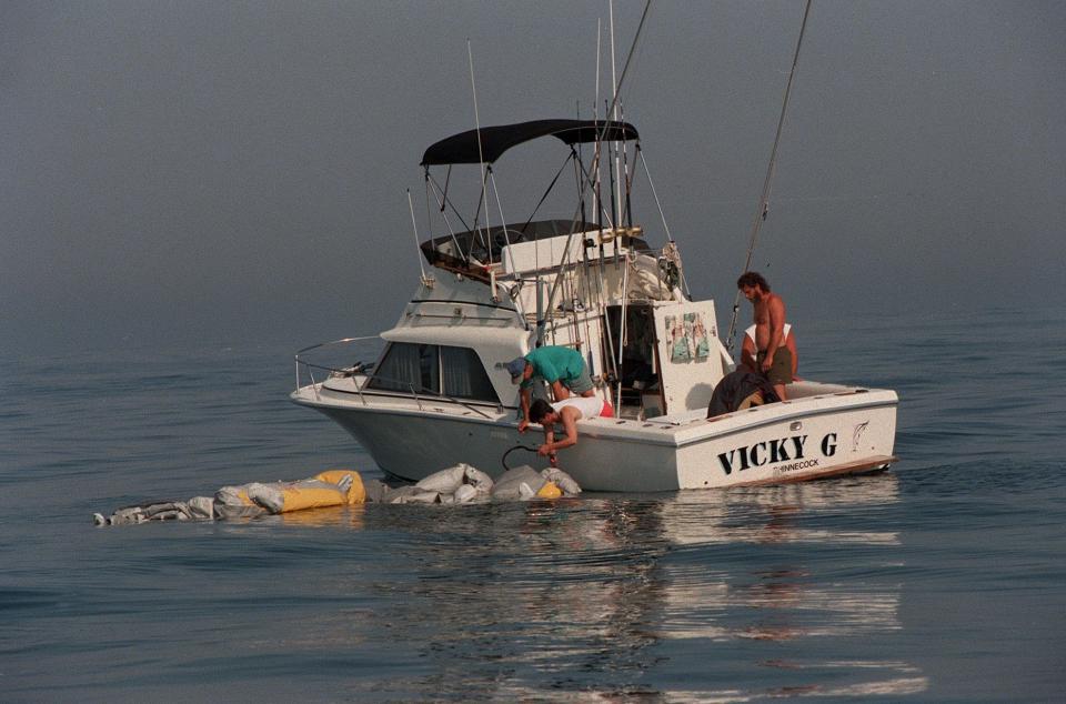 A group of men in a private boat struggle to haul what appears to be a life raft floating among the debris of the TWA crash, Thursday, July 18, 1996. Lots of personal crafts were assisting in the search. .