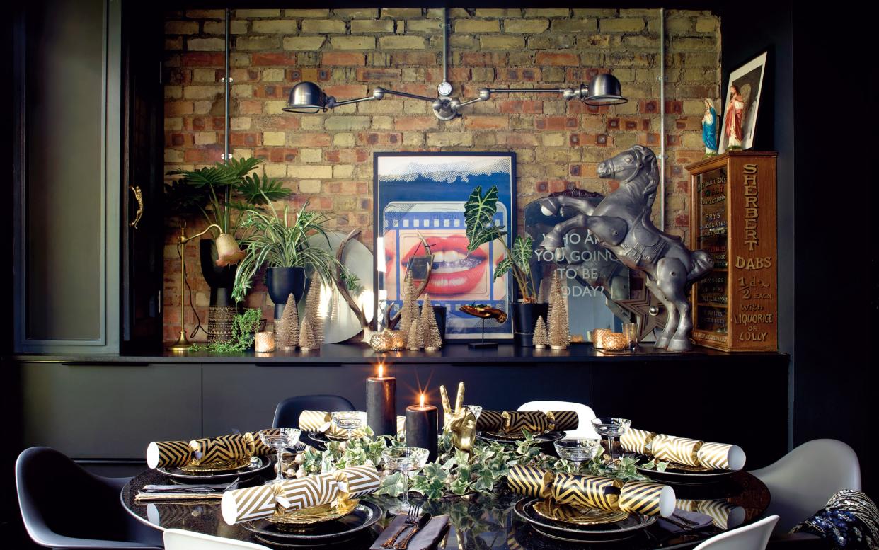 Industrial styling collides with glamour in the dining area, which is decorated in black and gold tones. The print is by Joe Tilson, while the antique mirror printed with the words, ‘Who are you going to be today?’ is from Vinegar & Brown Paper. A pair of kitsch Mary and Jesus figurines from Ardingly Antique Fair sit on top of the antique sweet cabinet. -  Claire Worthy