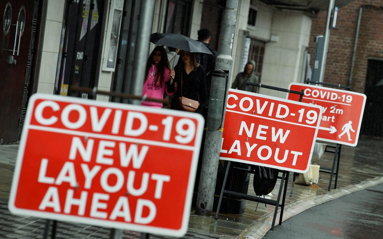 Shoppers are seen walking past social distancing signs following the outbreak of the coronavirus