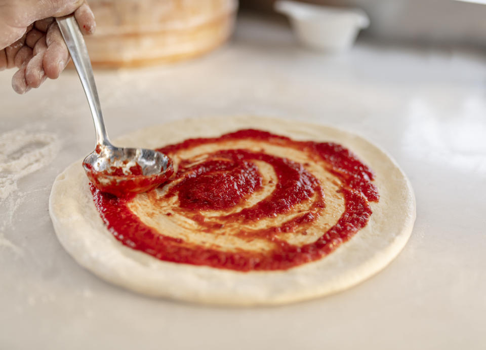 Spooning tomato sauce over an uncooked pizza