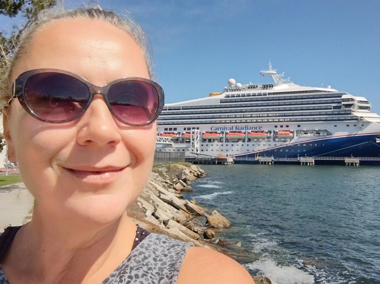 woman wearing dark sunglasses taking a selfie with a cruise ship