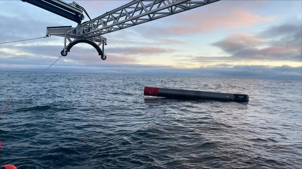 Eine zylindrische Rakete schwimmt auf einem ruhigen Ozean, während ein Kran sich darauf vorbereitet, sie von oben zu ergreifen