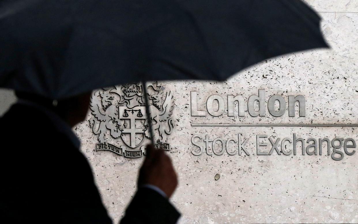 A man shelters under an umbrella as he walks past the London Stock Exchange in London