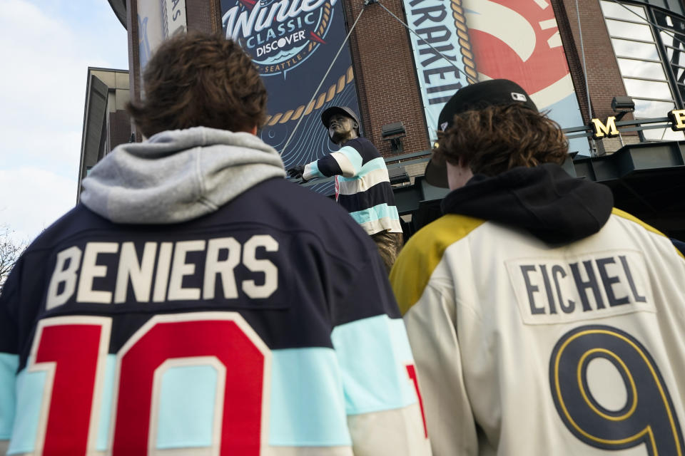 A fan in a Seattle Kraken's Matty Beniers jersey and a fan in a Vegas Golden Knights' Jack Eichel jersey stand in front of a statue of former Seattle Mariners player Ken Griffey Jr. wearing a Kraken jersey before the NHL Winter Classic hockey game Monday, Jan. 1, 2024, in Seattle. (AP Photo/Lindsey Wasson)