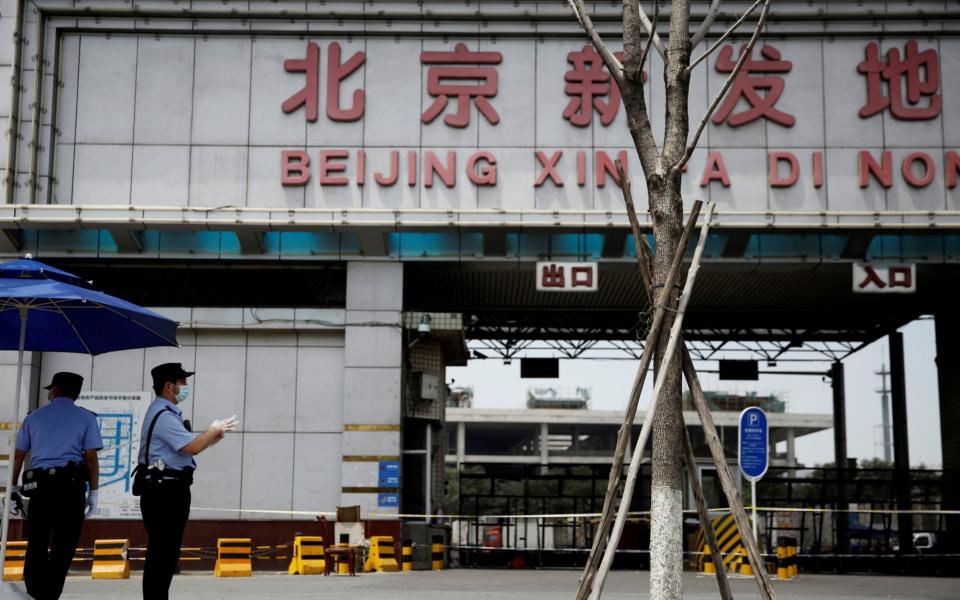 Police officers wearing face masks stand guard outside an entrance to the Xinfadi wholesale market in Beijing - REUTERS