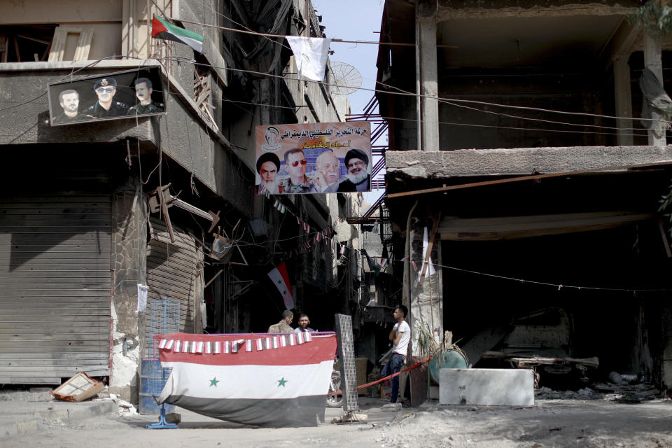 Men sit under a poster of the late Iranian revolutionary founder Ayatollah Khomeini, left, Syrian President Bashar Assad, second left, Head of the Popular Front for the Liberation of Palestine-General Command Ahmed Jibril, second right, and Hezbollah leader Sayyed Hassan Nasrallah at a check point in the Palestinian refugee camp of Yarmouk in the Syrian capital Damascus, Syria, Saturday, Oct. 6, 2018. The camp, once home to the largest concentration of Palestinians outside the territories housing nearly 160,000 people, has been gutted by years of war. (AP Photo/Hassan Ammar)