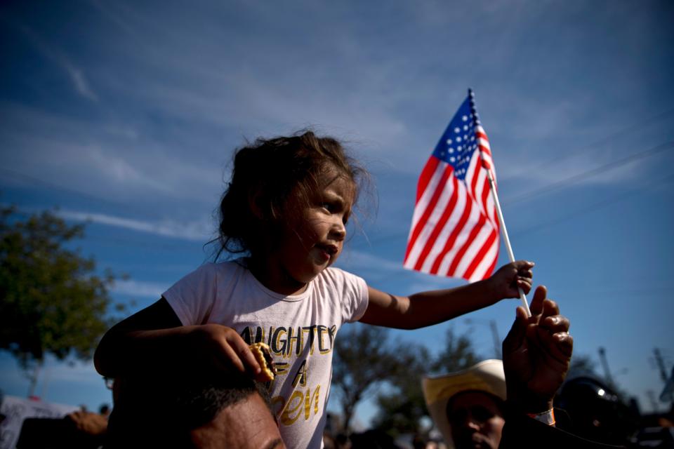 A migrant girl with a U.S. flag sits on the shoulders of a man marching with other migrants to the Chaparral border crossing in Tijuana, Mexico, on Nov. 25, 2018, as they try to reach the U.S.