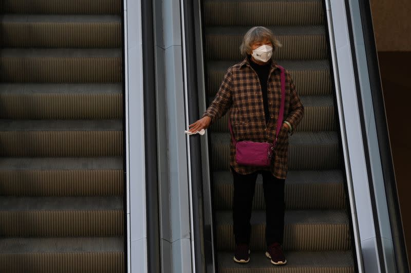 Woman wearing a face mask rides an escalator while holding onto the handrail with the use of a tissue, as she makes her way to a supermarket following an outbreak of the novel coronavirus in the country, in Kunming