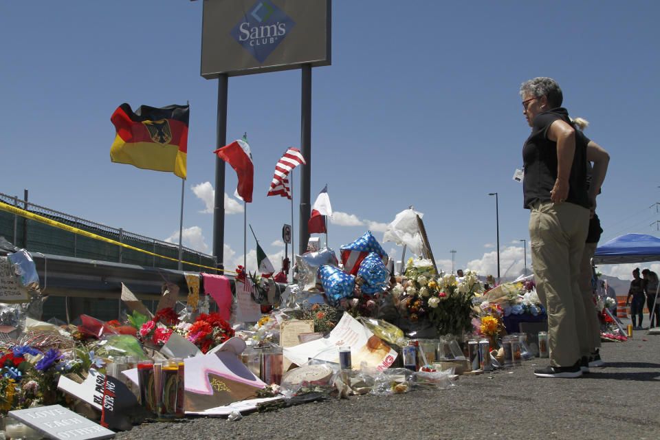 In this Aug. 12, 2019 photo, mourners visit the makeshift memorial near the Walmart in El Paso, Texas, where 22 people were killed in a mass shooting that police are investigating as a terrorist attack targeting Latinos. The flags show the nationalities of those killed in the attack, including a German man who lived in nearby Ciudad Juarez, Mexico. On Thursday, Aug. 22, 2019, Walmart said it plans to reopen the El Paso store where 22 people were killed in a mass shooting, but the entire interior of the building will first be rebuilt. (AP Photo/Cedar Attanasio)