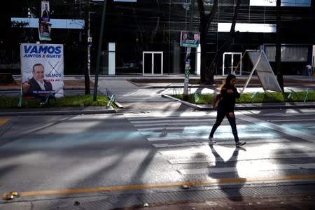 A woman cross a street by a campaign sign for Alejandro Giammattei, presidential candidate for the "Vamos" political party, ahead of the second round run-off vote, in Guatemala City