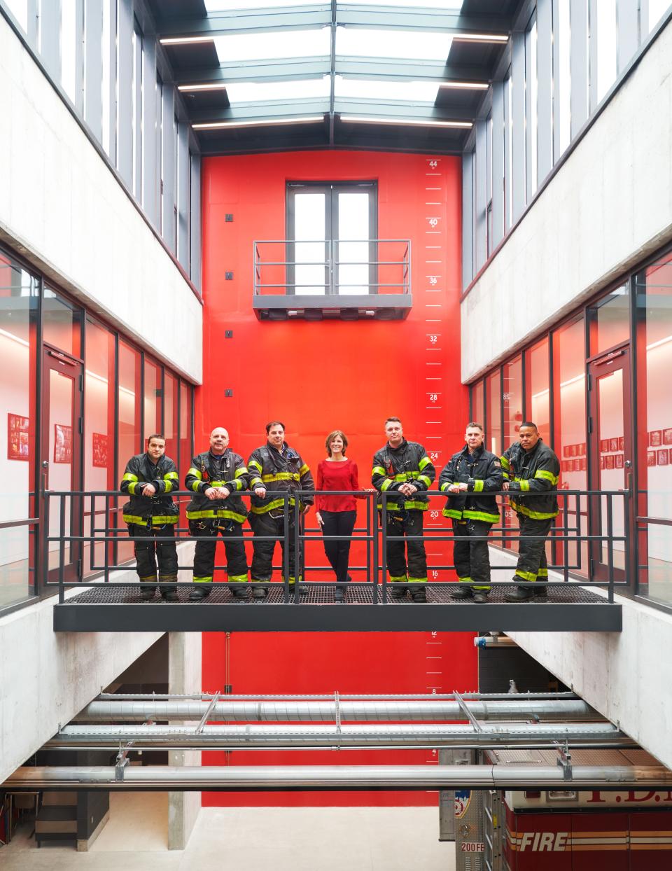Gang poses in the atrium with rescue workers; the climbing wall and balcony at rear are used to simulate missions.