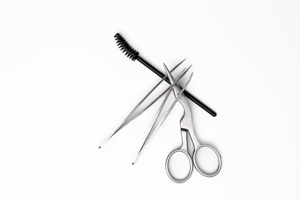 Scissors, tweezers and a spoolie brush, all tools that are used for how to tweeze eyebrows