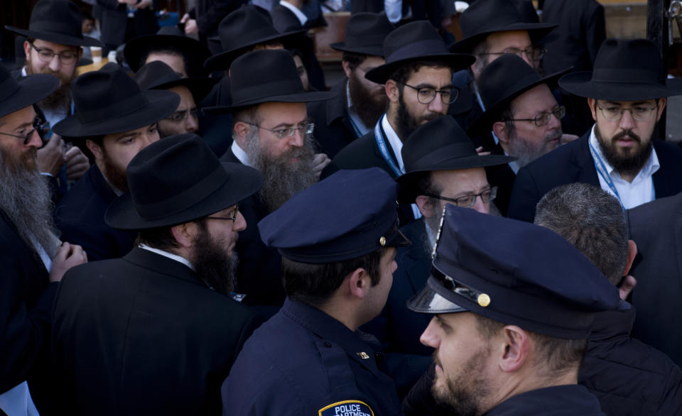 In this Sunday, Nov. 4, 2018, photo New York City police officers watch as rabbis gather for a group photo at the Chabad-Lubavitch World Headquarters in New York. More than 5,000 of the orthodox Jewish leaders are taking part in the annual meeting. The NYPD has increased patrols at houses of worship in light of the recent fatal shooting at a synagogue in Pittsburgh. (AP Photo/Mark Lennihan)