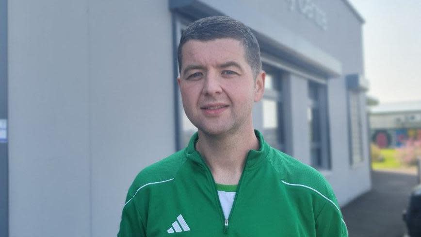 Gary Clarke in a green and while sports top standing in front of a grey building