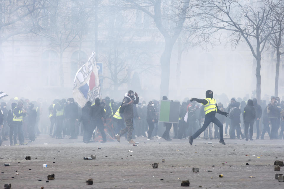 A yellow vests demonstrator throws an item to police officers, Saturday, March 16, 2019 in Paris. French yellow vest protesters clashed Saturday with riot police near the Arc de Triomphe as they kicked off their 18th straight weekend of demonstrations against President Emmanuel Macron. (AP Photo/Christophe Ena)