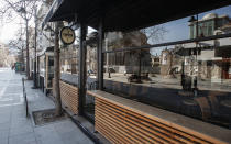 People sitting on benches in a usually crowded street are reflected in the window of a closed restaurant in downtown Skopje, North Macedonia, Wednesday, March 18, 2020. While expecting the President to declare the state of emergency, North Macedonia has closed borders for foreign nationals to enter, shut down two country's airports, restaurants, bars, schools, universities, kindergartens and constantly appeal people to stay at home to slow the spread of the coronavirus outbreak. For most people, the new coronavirus causes only mild or moderate symptoms. For some it can cause more severe illness, especially in older adults and people with existing health problems. (AP Photo/Boris Grdanoski)