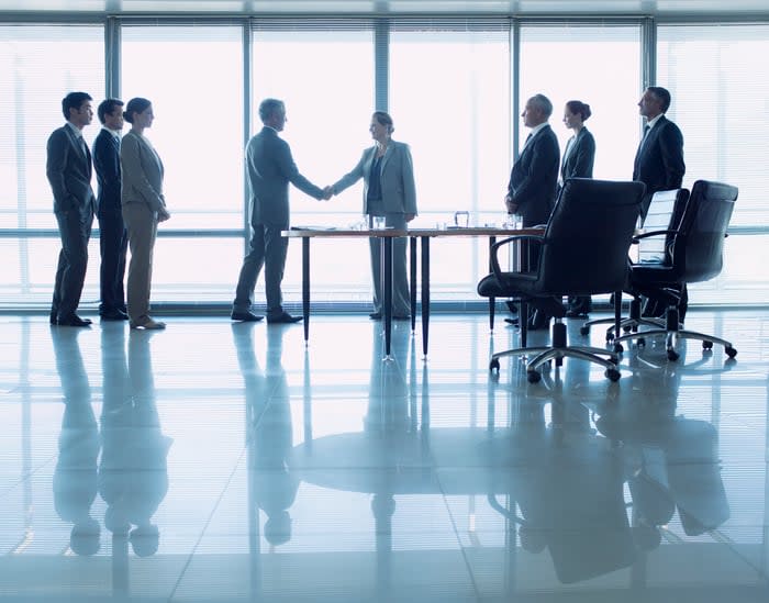 Professionals shake hands in a conference room.