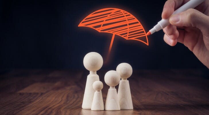 Wooden figurines representing family and hand drawing umbrella, symbol of insurance.