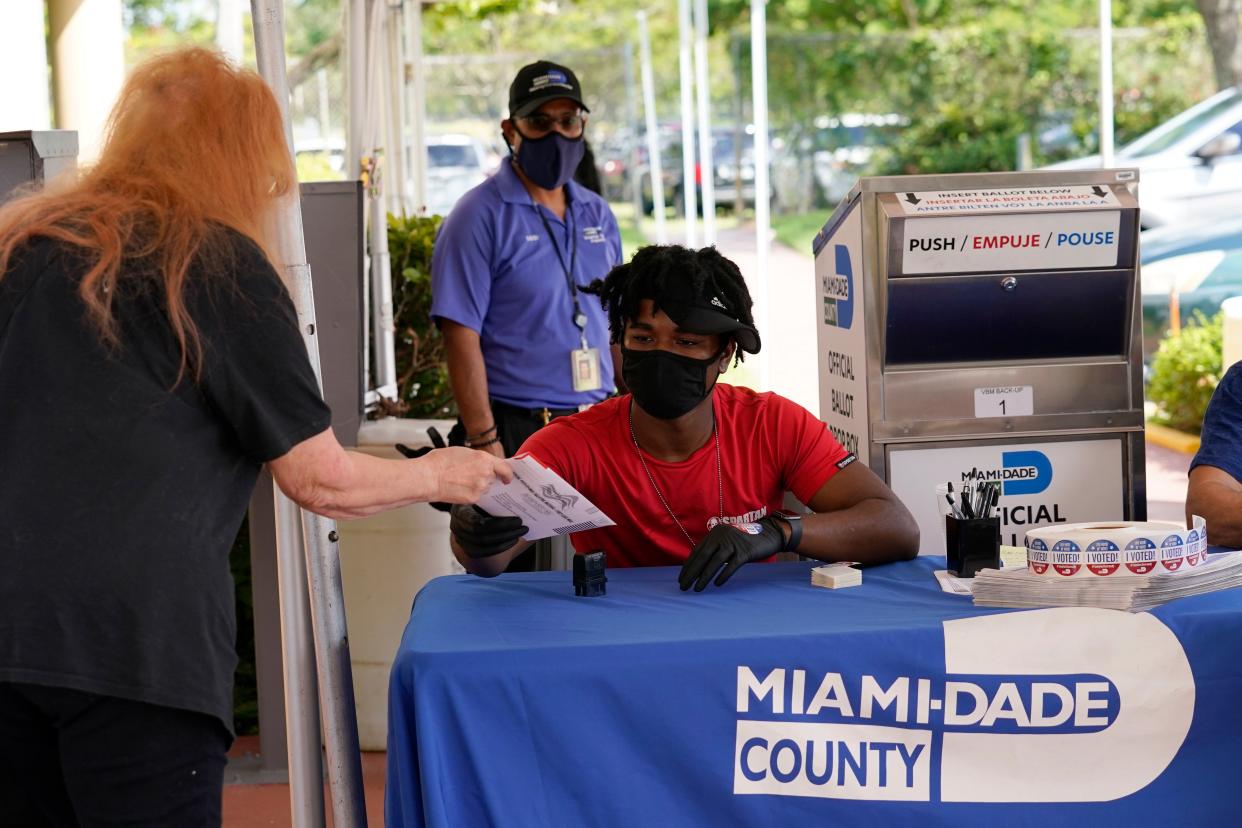 Election worker Najeh Fisher, right, takes a vote-by-mail ballot to place into an official ballot drop box at the Miami-Dade County Elections Department on 14 October in Florida. (AP)