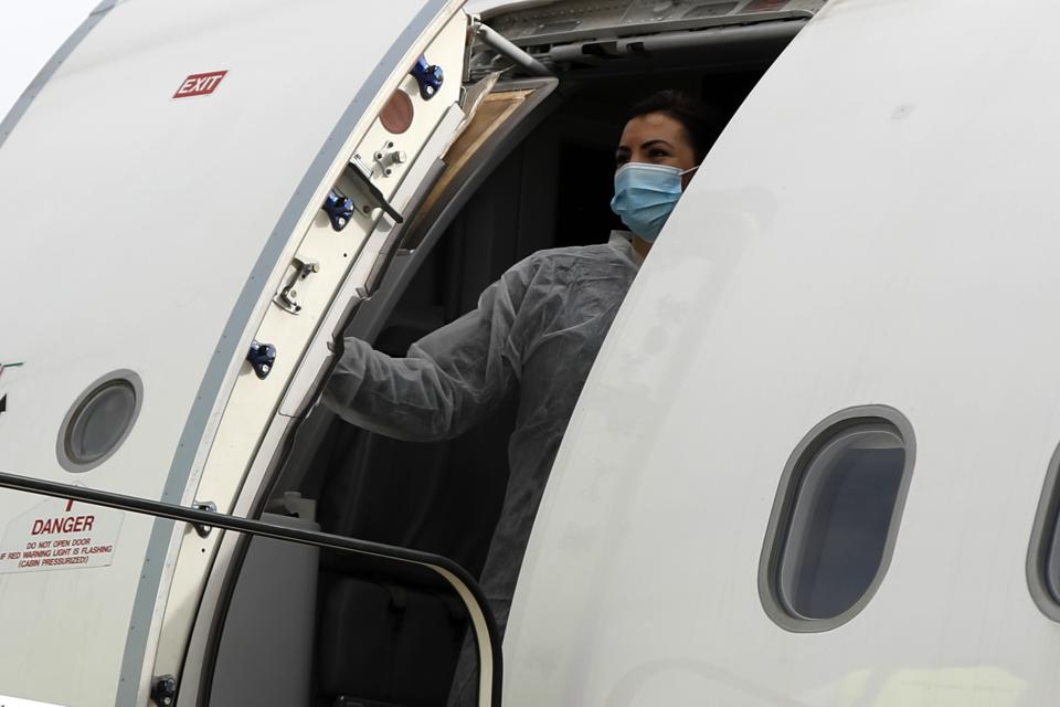 An air hostess wearing protective suit and face mask to protect form the spread of the coronavirus, closes the door of the aircraft after the boarding of migrants bound for Britain at the Eleftherios Venizelos International Airport in Athens, on Monday, May 11, 2020. Sixteen asylum-seeking minors and 34 migrants were relocated as part of a migrant reunification plan agreed between the two countries. (AP Photo/Thanassis Stavrakis)