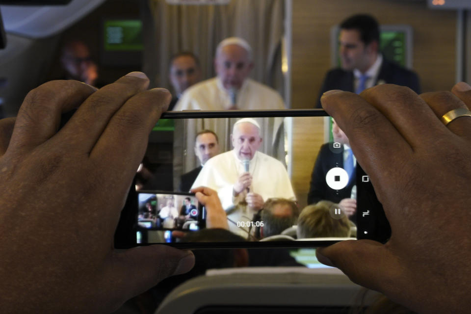 Pope Francis is framed in a smartphone as he greets journalists aboard an airplane on his way to the United Arab Emirates, Sunday, Feb. 3, 2019. Francis made an urgent appeal for an end to the humanitarian crisis in Yemen on Sunday as he embarked on the first-ever papal trip to the Arabian Peninsula, where he is seeking to turn a page in Christian-Muslim relations while also ministering to a unique, thriving island of Catholicism. (AP Photo/Andrew Medichini)