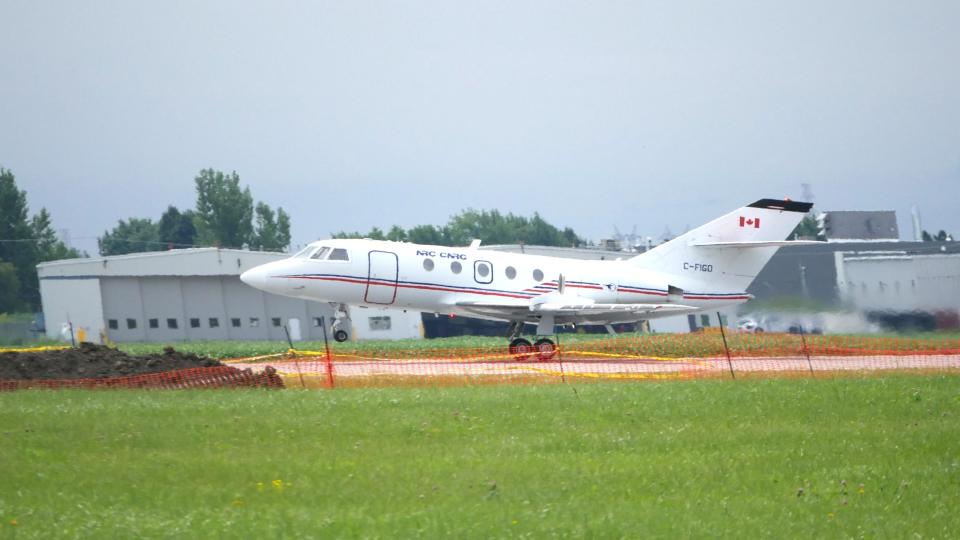 a long business jet taking off from a runway. Grass and construction fences stand in front of it