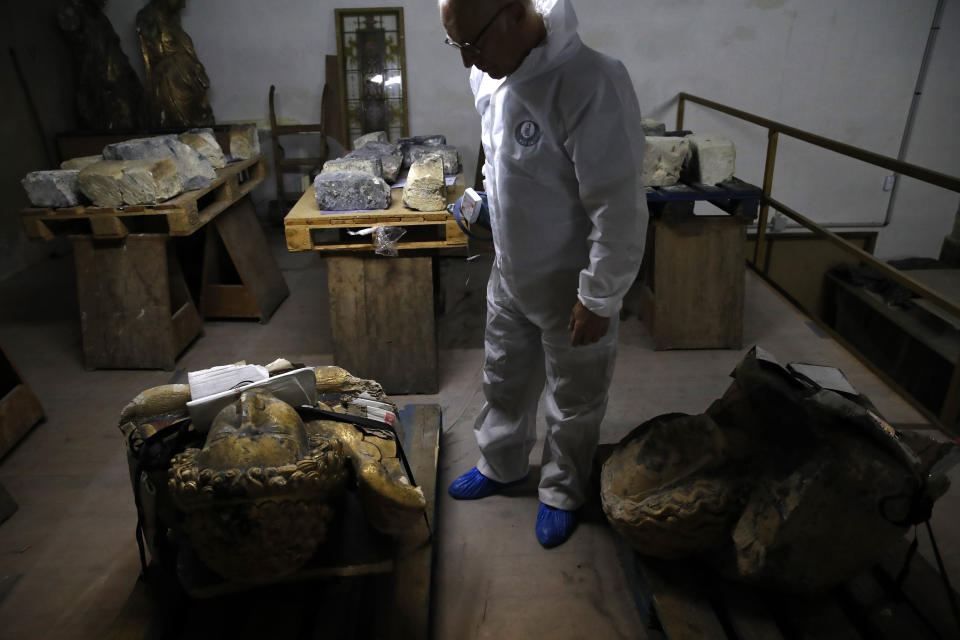 In this photo taken on Wednesday, Oct. 9, 2019, stone expert Jean-Didier Mertz, looks on next to the remains of the golden angel that was once atop Notre Dame cathedral, in a warehouse at Champs-sur-Marne, west of Paris. Scientists at the French government's Historical Monuments Research Laboratory are using these objects as clues in an urgent and vital task, working out how to safely restore the beloved Paris cathedral and identify what perils remain inside in a race against the clock. (AP Photo/Francois Mori)