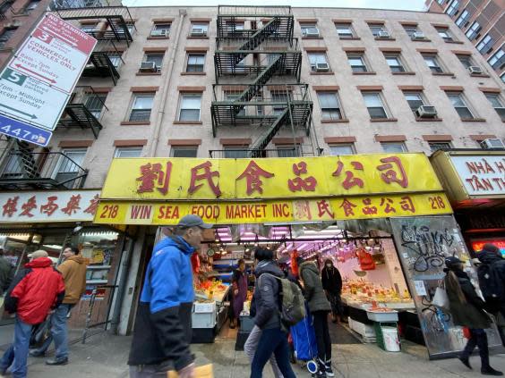 Pedestrians pass by outside of a Chinatown fish market (Clark Mindock/The Independent)