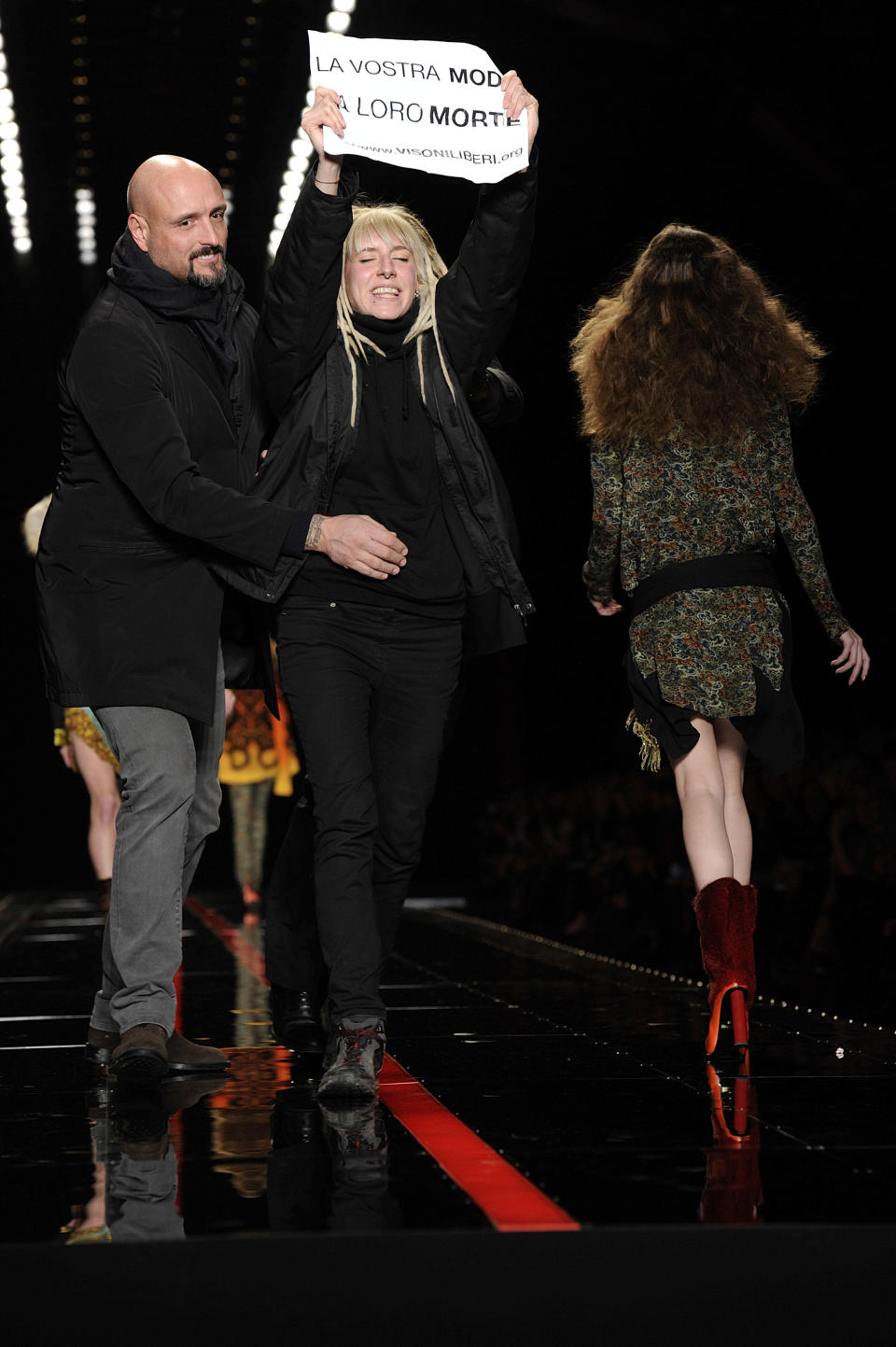 A security guard stops an animal rights activist walking on the catwalk with a placard reading in Italian "La vostra moda la loro morte" (Your fashion their death) during the show of the Just Cavalli women's Fall-Winter 2013-14 collection, part of the Milan Fashion Week, unveiled in Milan, Italy, Thursday, Feb. 21, 2013. (AP Photo/Giuseppe Aresu)
