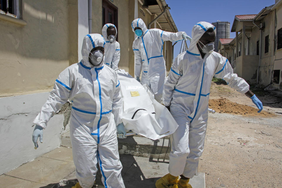 In this photo taken Wednesday, May, 13, 2020, medical workers in protective suits carry the body of Ibrahim Hassan, 56, before he is buried in Mogadishu, Somalia. His brother said he died of the coronavirus at the Martini Hospital. At the hospital, the main facility treating COVID-19 patients in Mogadishu, health care workers have received little training, and they have raised concerns about their personal safety. (AP Photo/Farah Abdi Warsameh)