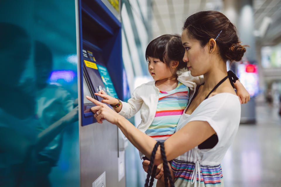 Pretty young mom carrying lovely little girl using an automatic teller machine together in the train station