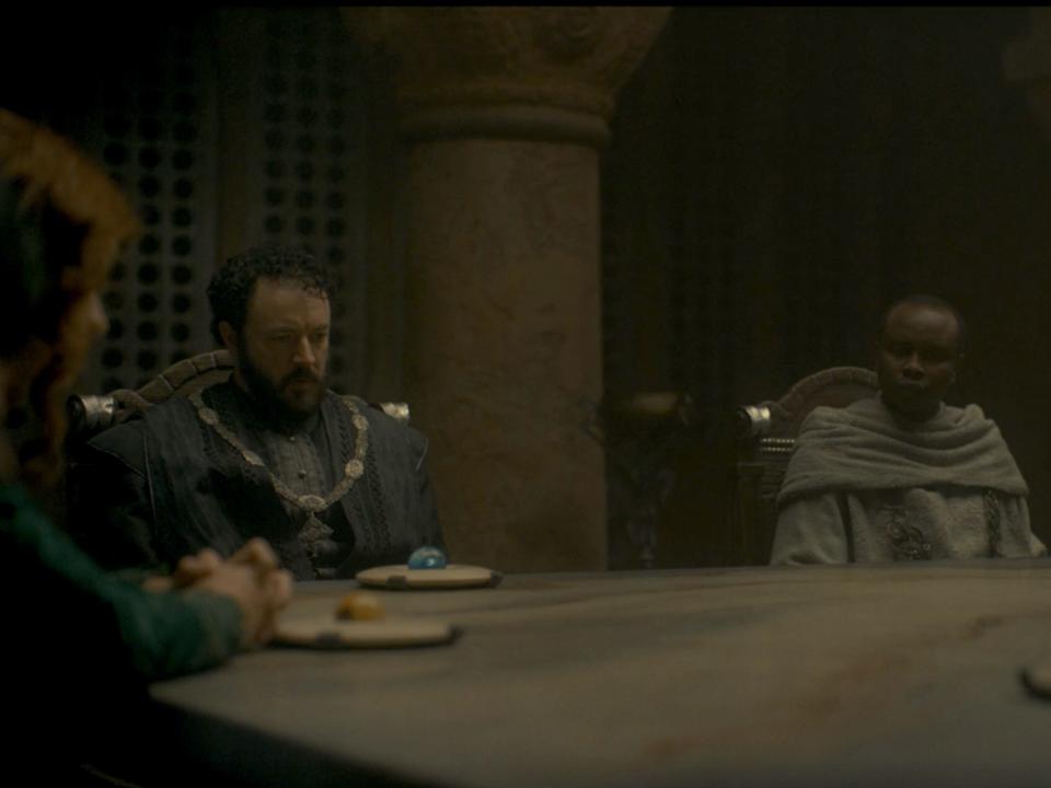 Three men sit at a table with serious looks on their faces.