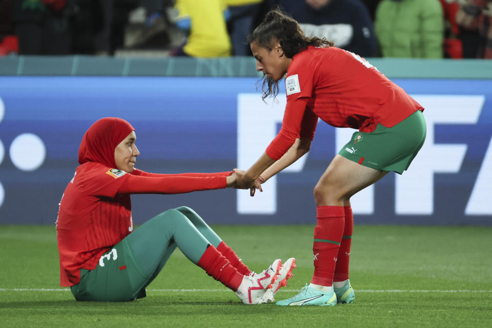 Morocco's Nouhaila Benzina, left, is helped to her feet by teammate Sarah Kassi following the Women's World Cup round of 16 soccer match between France and Morocco in Adelaide, Australia, Tuesday, Aug. 8, 2023. (AP Photo/James Elsby)