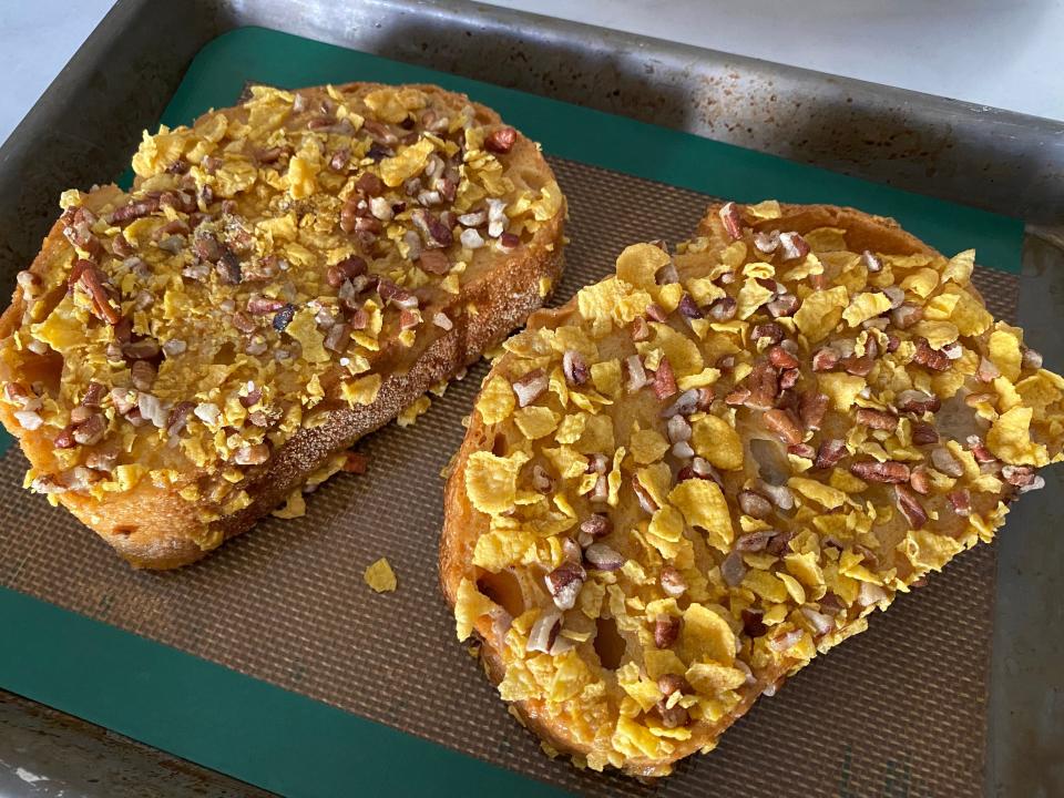 Two slices of uncooked french toast covered in cornflakes and pecans on a baking tray