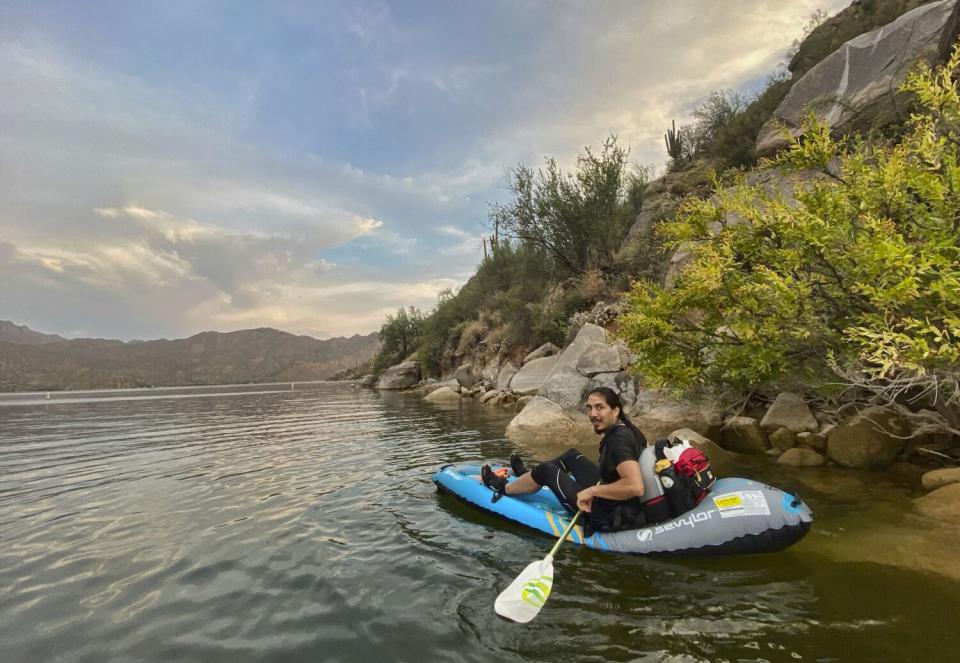 A young man paddles on a calm river, sitting on an inflatable kayak.