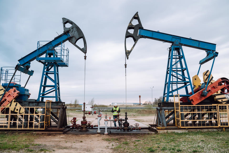 Silhouettes of onshore oil and gas wells in the field outdoors against blue cloudy sky.