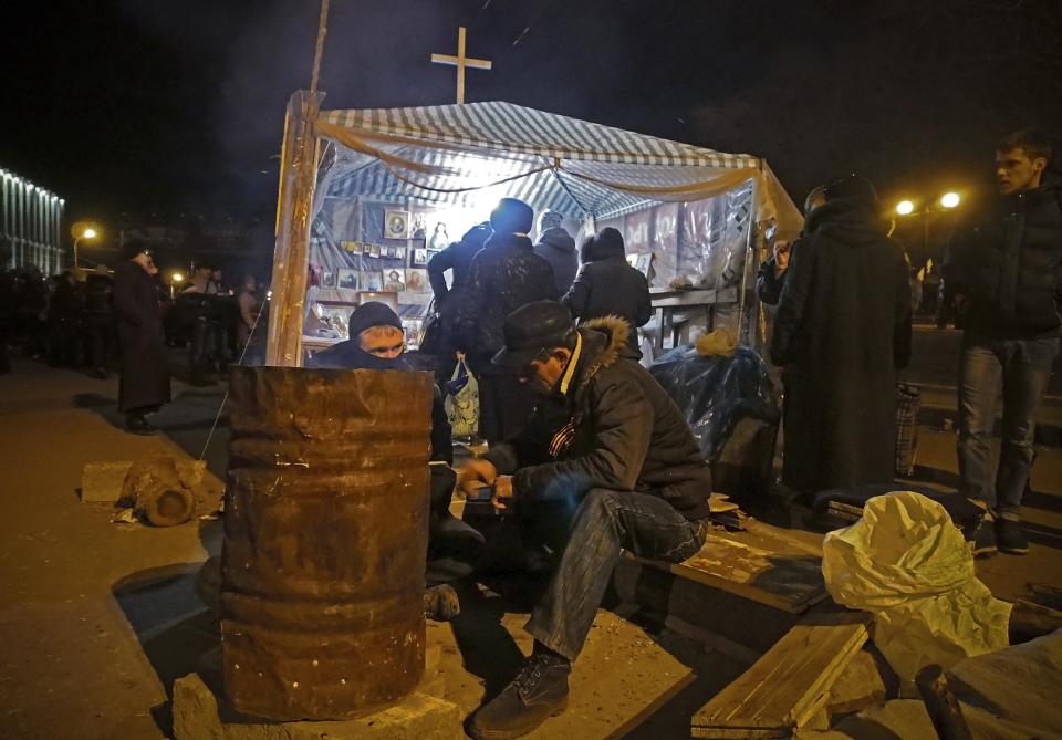 A man warms himself at a fire next to barricades in front of an entrance of the Ukrainian regional office of the Security Service in Luhansk, 30 kilometers (20 miles) west of the Russian border, in Luhansk, Ukraine, late Saturday, April 12, 2014. Ukrainian Interior Minister Arsen Avakov described the unrest as "Russian aggression" and said Ukraine's security officials would be gathering for an extraordinary meeting late Saturday evening. (AP Photo/Igor Golovniov)