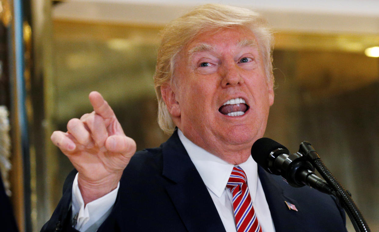 Then-President Donald Trump speaks into a microphone and points his finger outward as he responds to reporters' questions.