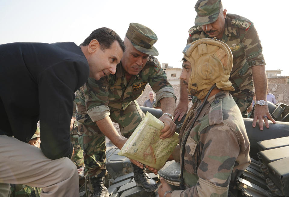 In this photo released on the official Facebook page of the Syrian Presidency, Syrian President Bashar Assad, left, speaks with Syrian troops during his visit to the strategic town of Habeet, in the northwestern province of Idlib, Syria, Tuesday, Oct. 22, 2019. On Tuesday, Assad called the Turkish President Recep Tayyip Erdogan a "thief" during his first visit to territory captured from Turkey-backed rebels in the northwestern province of Idlib. (Facebook page of the Syrian Presidency via AP)