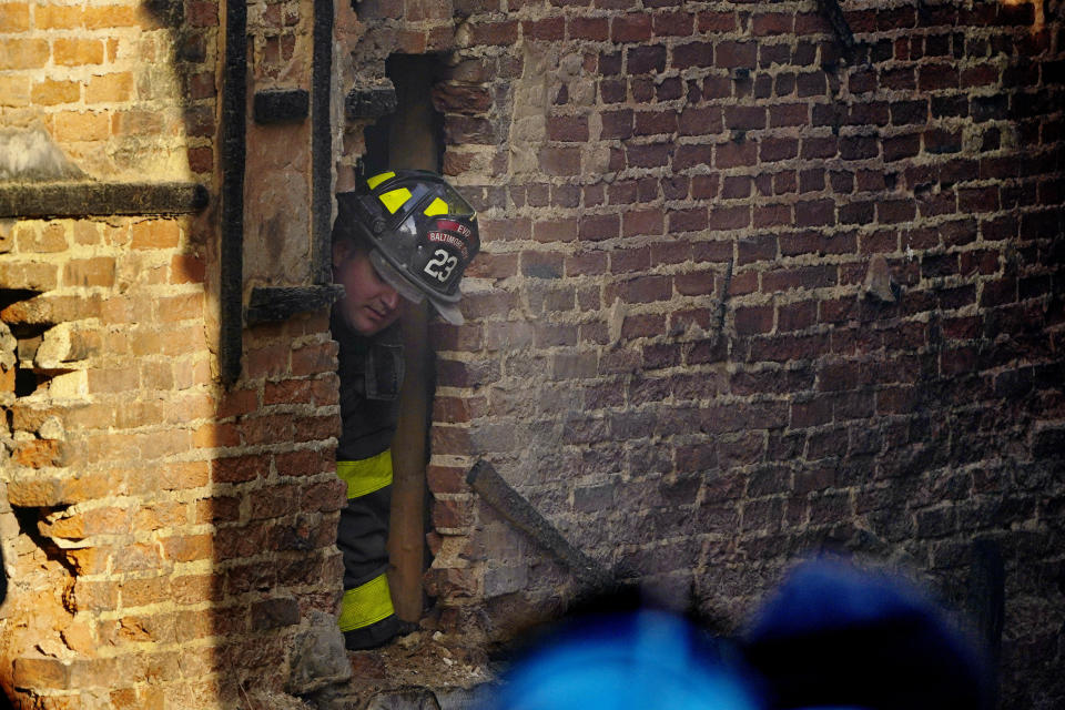 A fire official looks through a hole in a wall as officials try to retrieve the body of a deceased firefighter trapped in a building collapse while battling a two-alarm fire in a vacant row home, Monday, Jan. 24, 2022, in Baltimore. (AP Photo/Julio Cortez)