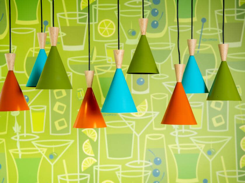 Colorful pendant lights hang in front of a lime green wall decorated with drawings of cocktails