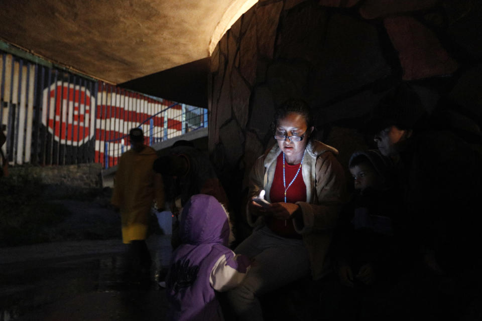 Honduran migrant Leivi Ortega, 22, wearing a rosary, looks at her phone while she, her partner and their young daughter, wait in hopes of finding an opportunity to cross the U.S. border from Playas de Tijuana, Mexico, Wednesday, Dec. 5, 2018. In early December, U.S. Customs and Border Protection said that the San Diego sector experienced a "slight uptick" in families entering the U.S. illegally with the goal of seeking asylum. (AP Photo/Rebecca Blackwell)