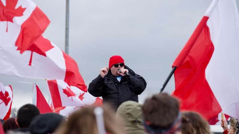 A man addresses a crowd waving Canadian flags, in protest of COVID-19 vaccine mandates.