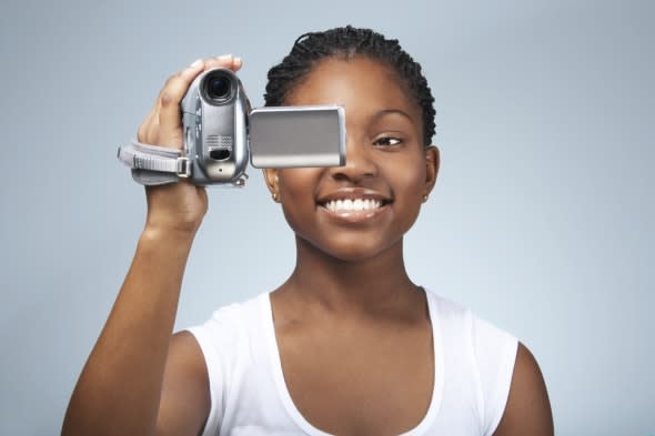 Teenage girl (15-17) using video camera, smiling, close-up