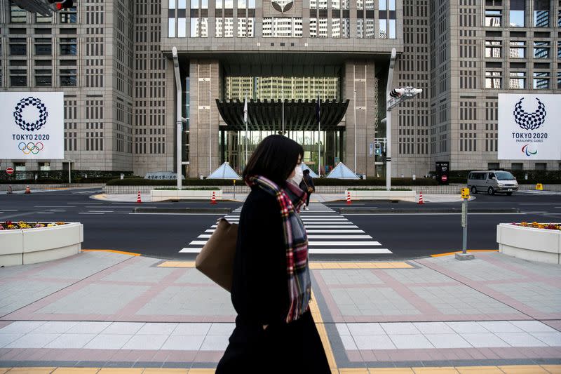 FILE PHOTO: A woman wearing a protective face mask, following an outbreak of the coronavirus, walks past banners of the upcoming Tokyo 2020 Olympic and Paralympic Games outside the Tokyo Metropolitan Government building in Tokyo