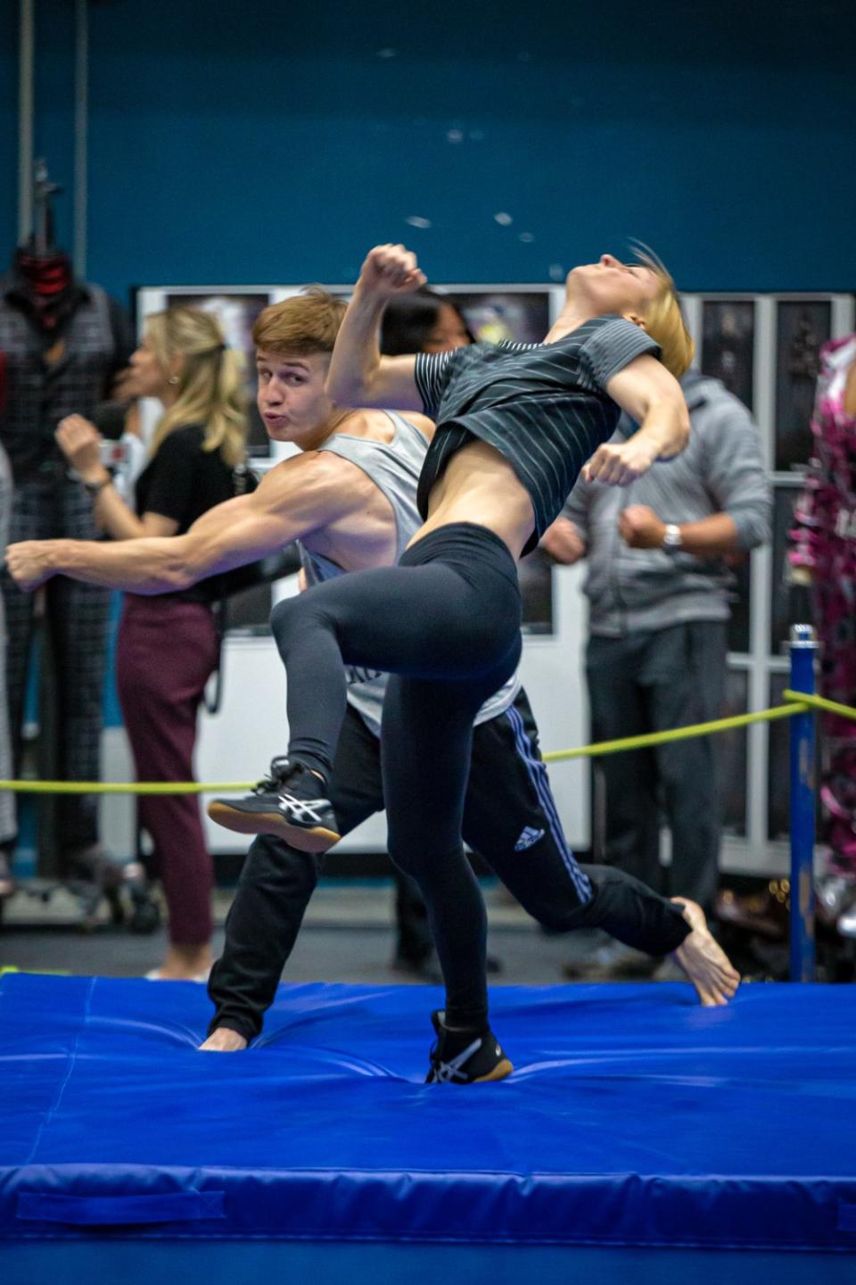 Actors practice stunts on a blue exercise mat.