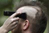 Kris Adey cuts the hair of her husband Danny Christian into a mohawk in front of their Takoma Park, Md., home, Tuesday, April 14, 2020. The couple hatched a plan disguised as a "crazy head day" haircut for a spirit week contest with Christian's telework colleagues to announce that the couple was expecting their first child. Christian, who dyed the mohawk blue, won the competition. Since barbershops and hair salon's are closed because of the coronavirus pandemic, some people are letting those in their isolation bubble cut their hair. (AP Photo/Susan Walsh)