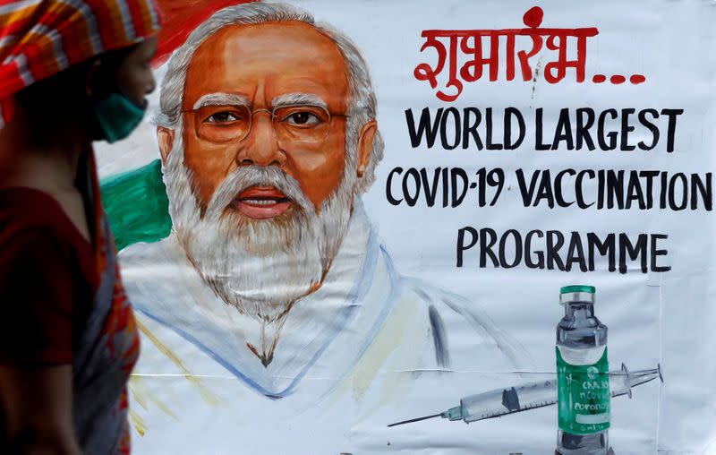 A woman walks past a painting of Indian Prime Minister Narendra Modi a day before the inauguration of the COVID-19 vaccination drive on a street in Mumbai