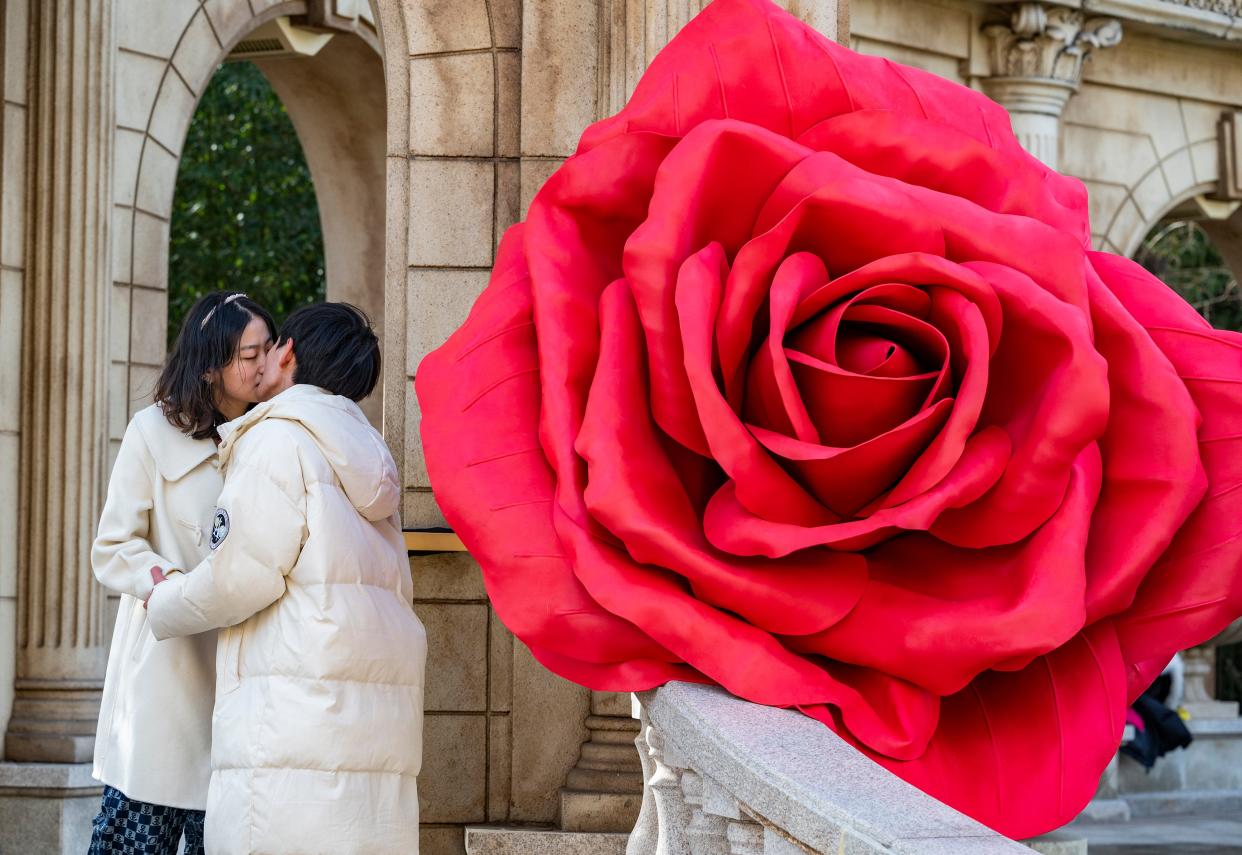 A couple kisses next to an installation display of red roses before Valentine's Day on February 13, 2023 in Beijing, China.