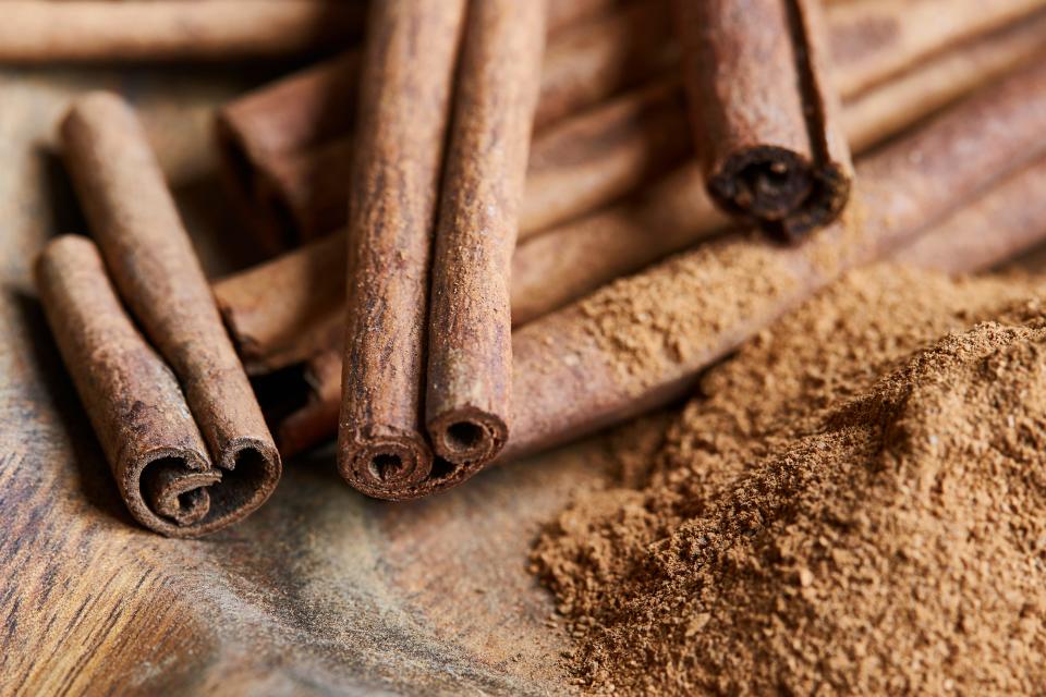 Cinnamon sticks and powder in a handmade wooden bowl on an oak wooden table top.